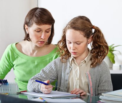 Teenager girl sitting together with her mother and showing her homework