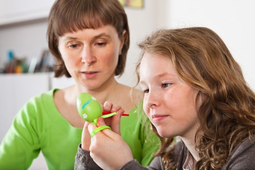 Mother and daughter sitting at home together and painting easter eggs
