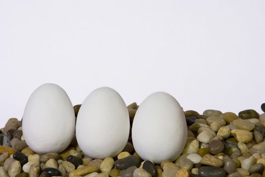 Three white easter eggs on pebbles against white background