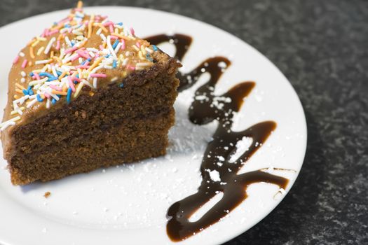 Rich moist chocolate cake on a white plate with grey background