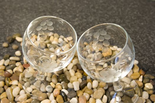 Two wine glasses on pebbles set against grey background