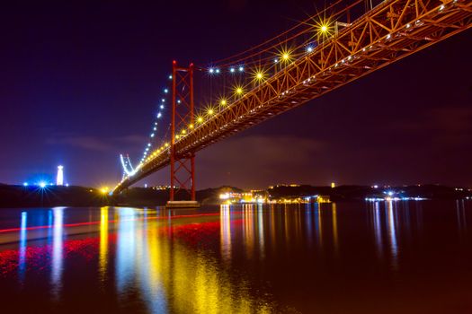 The 25 de Abril Bridge - suspension bridge over the river Tagus illuminated at night. Lisbon Portugal