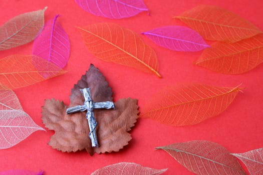 Silver cross made from wood amongst autum leaves
