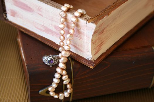 Pearls and a silver ring with a purple stone on a wooden jewellery box