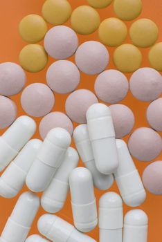 Macro view of white pink and orange pills on orange background.