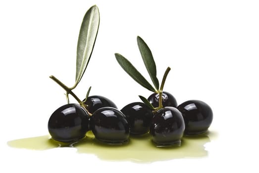 Premium black olives with leaves covered in olive oil and isolated over a white background.