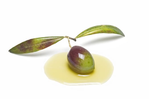 Green olive with leaves on some olive oil and isolated over a white background.