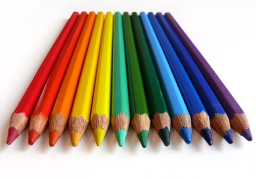 Rainbow colored pencils lying on white paper