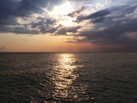 Evening at the sea with sun, clouds and reflection in water