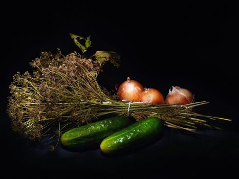 A punch of dill, two cucumbers and tree onions lying on the black background