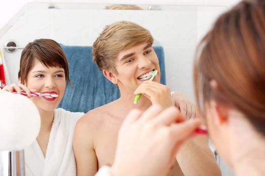 Young couple cleaning teeth together at bathroom. Focus on man.