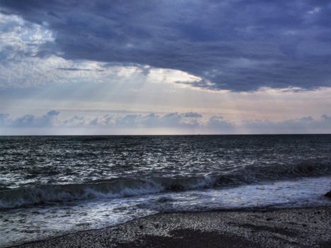 Cloudy beach sunset with waves and pebble shore