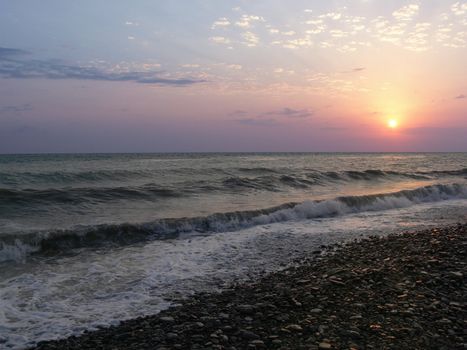 romantic beach sunset with waves and pebble shore