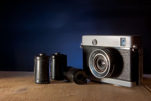 The camera and films on a wooden surface against a dark background