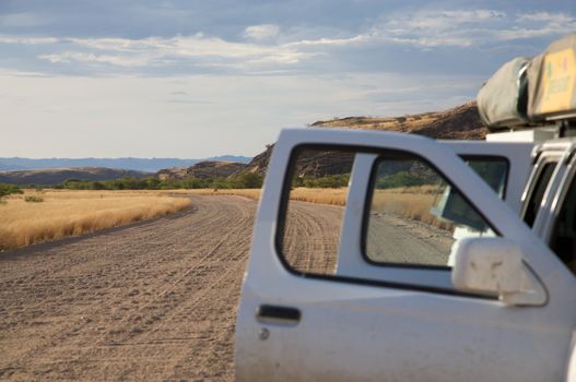 Car with the doors open  on track in Namibia late afternoon with focus on landscape