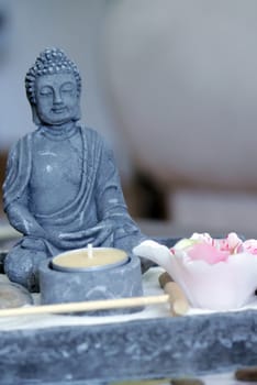 Grey stone buddha in front of a small yellow candle on a zen table