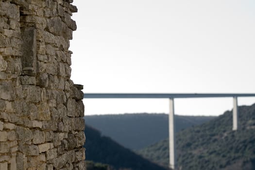 Photo of a old stone house ruins and a new high bridge in the background