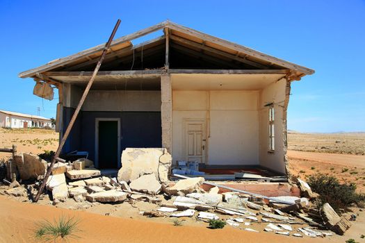 Abandoned house in Kolmanskop in Namibia with a blue sky and the desert of sand all around