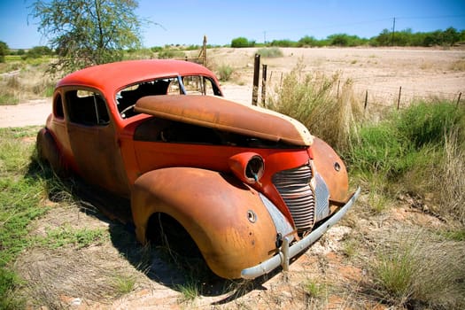 A wide angle view of a rusty old abandoned car under puffy blue skies in the Game Reserve of Central Kalahari in Botswana