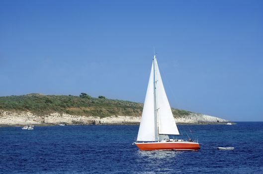 Red sailboat sailing between small islands