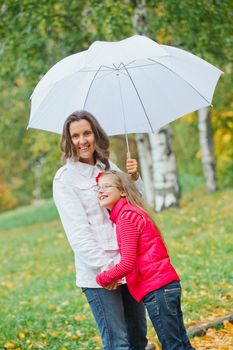 Cute girl with her mother with white umbrella walking in the autumn park. Rain, yellow leaves, tree.