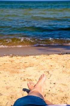 Woman in jeans skirt with crossed legs resting on the beach

