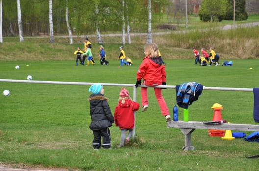 Three girls watching soccer practice.