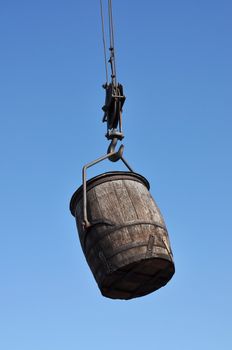 Old wooden barrel hanging in a hock against blue sky.