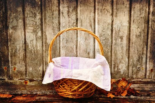 Picnic basket with autumn leaves aganst an old wooden wall.