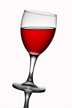 Leaning wine glass with red wine. With reflections in the white background