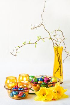 Easter decoration with daffodils, chocolate eggs and yellow glass-ware