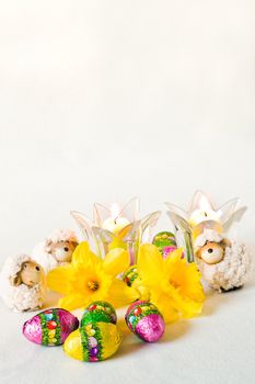 Easter decoration with sheep, chocolate eggs, daffodils and candles - vertical