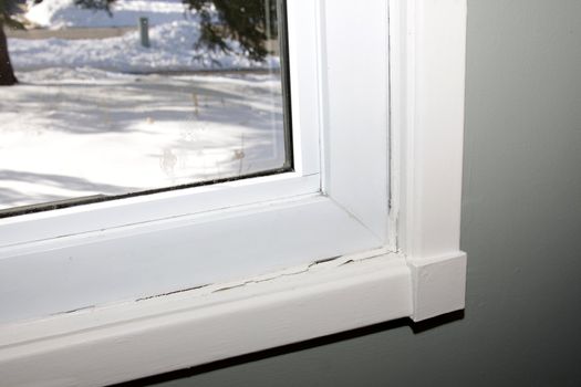 A window with damaged caulking, shot with snow visible through the window.
