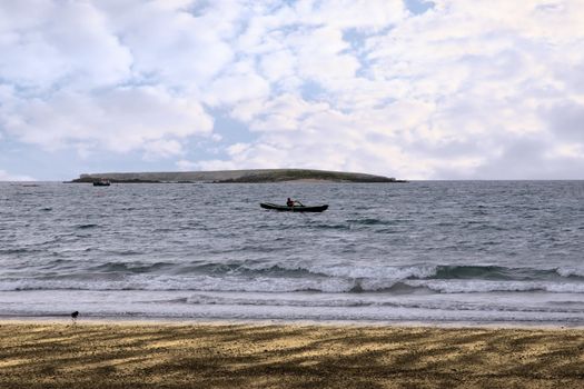a single rower in an ancient traditional irish curragh boat near a beach on the west coast of ireland