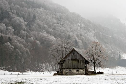 Old barn in snowy field.