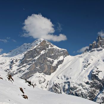 Photo of a mountain and a fluffy white cloud on deep blue sky in the Swiss Alps.