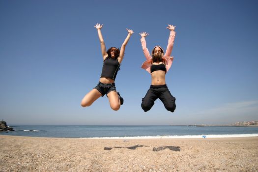 girls jumping on the beach with blue sky