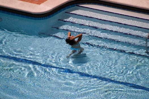 Woman in Pool was captured with her hands brushing her hair back as she starts to emerge from the blue water.
