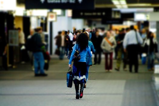 Female Airline Passenger is walking down the concourse. She is wearing a blue outfit that shimmers with every step. She has red on the bottom of her shoes that appear as she walks. An artistic blur has been applied to highlight her focal path in this airport terminal.
