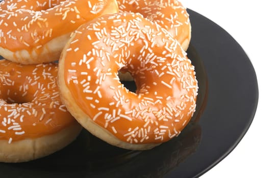 Orange glazed donuts with white sprinkles on a black plate isolated on a white background.
