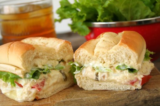 Fresh tuna salad sandwich on a hoagie roll with ice tea and a bowl of lettuce in the background.