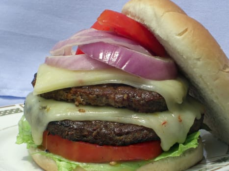 A serving of a thick, juicy and nutritious hamburger with vegetables and a melted cheese.