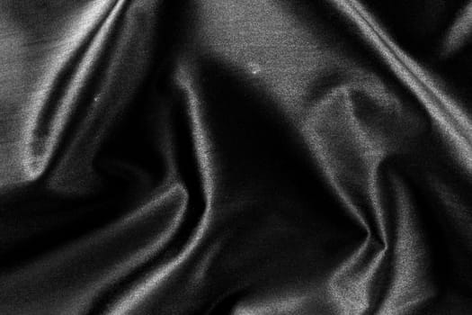 A background of a crumpled black shiny fabric.