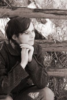 Beautiful brunette female sitting against a worn fence