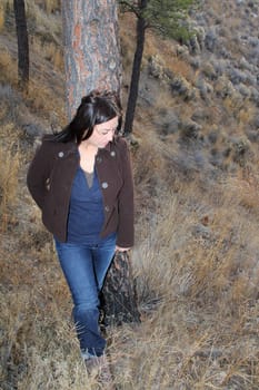Mature brunette female leaning against a tree