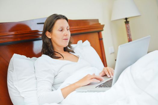 Smiling woman using laptop computer at home sitting in bed