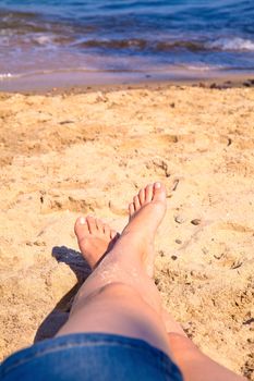 Woman in jeans skirt with crossed legs resting on the beach
