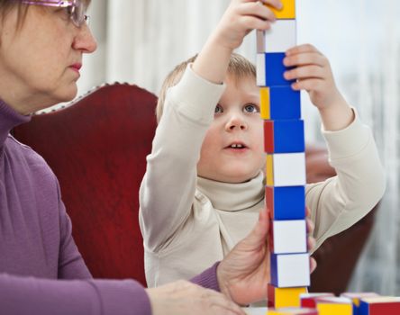 Little blond boy is building tower from colorful blocks