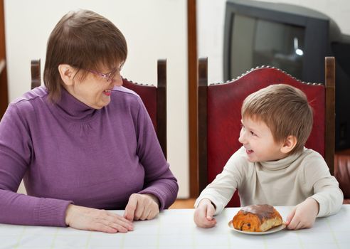 Smiling grandson and his granny sitting at the table at home