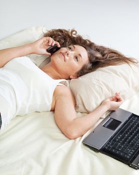 Undressed young woman lying in bed and talking on cellphone